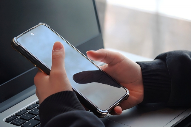 携帯を操作する手元とノートパソコン
