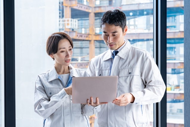 ノートパソコンの画面を確認する作業服の男女