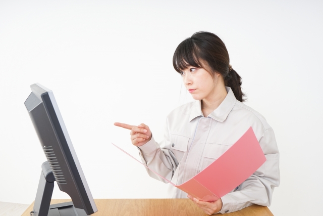 ノートパソコンを指差して確認する作業服の女性