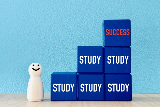 「STUDY」のブロック上に乗る「SUCCESS」のブロックと、笑顔の人形