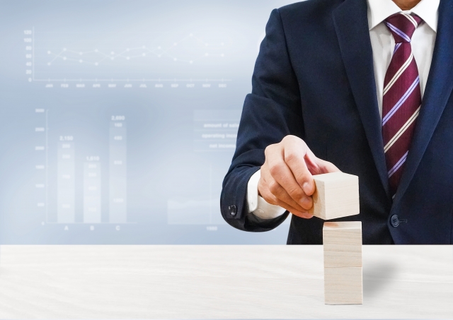 積み木を重ねるビジネスマンとグラフ背景